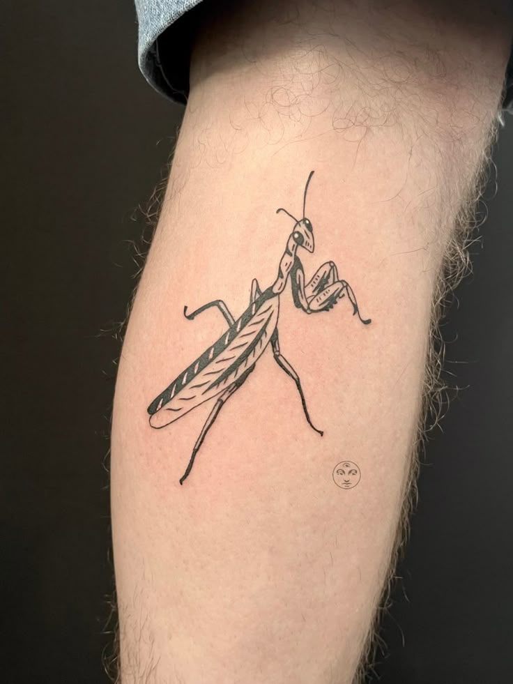 a man's leg with a small tattoo of a praying bug on the thigh