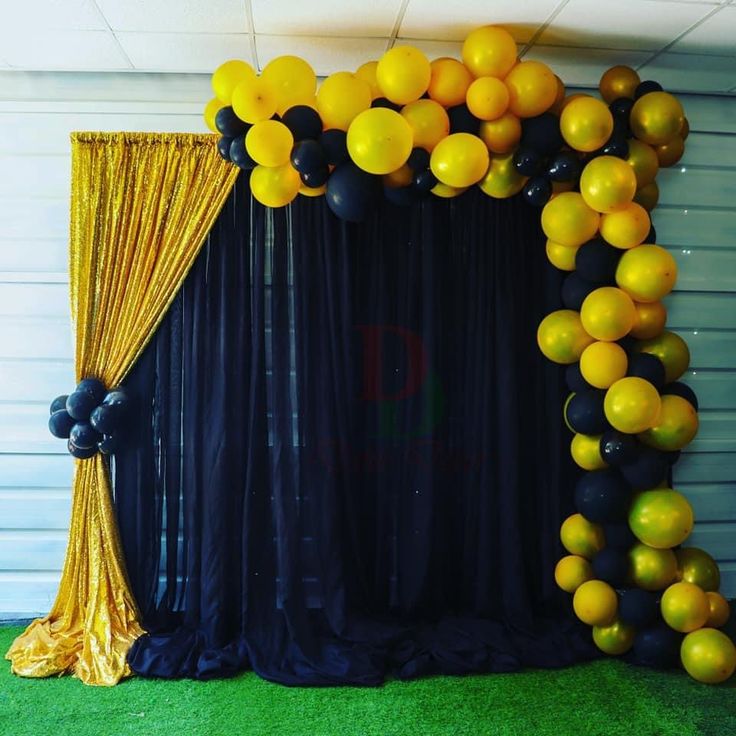 a black and gold balloon arch with yellow balloons on the top, along with an orange curtain