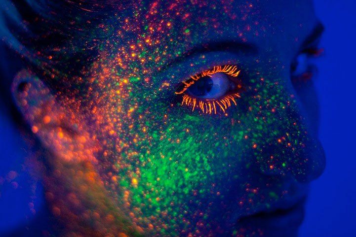 a woman's face is covered in glitter and has her eyes glowing green, red, yellow and blue