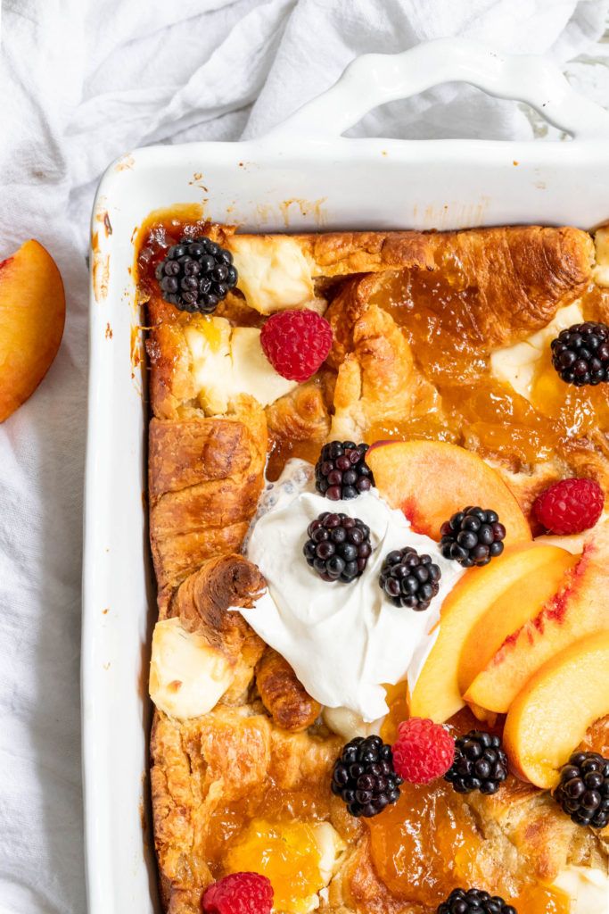 a casserole with fruit and whipped cream on top is sitting in a white dish