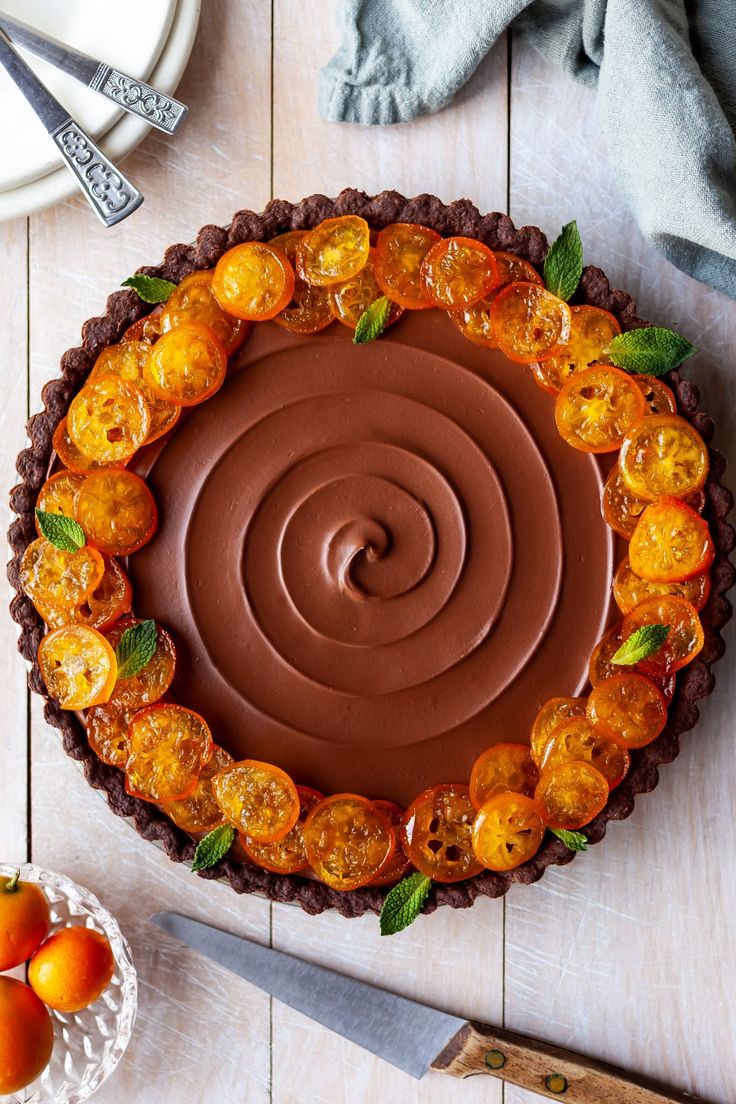 a chocolate tart with oranges in the middle on a wooden table next to a knife