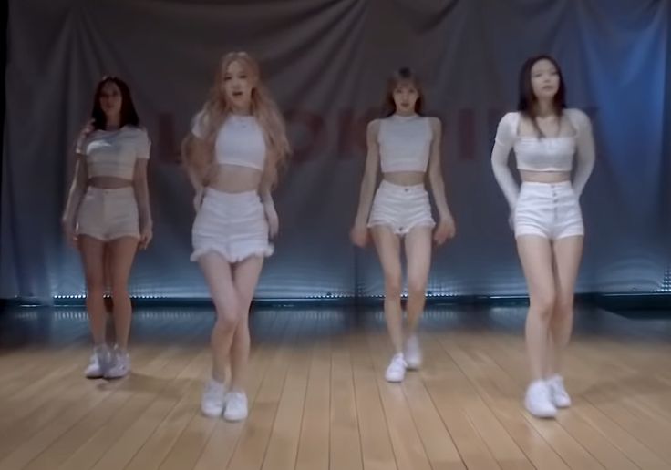 four women in short skirts are standing on a wooden floor and one is wearing white shoes