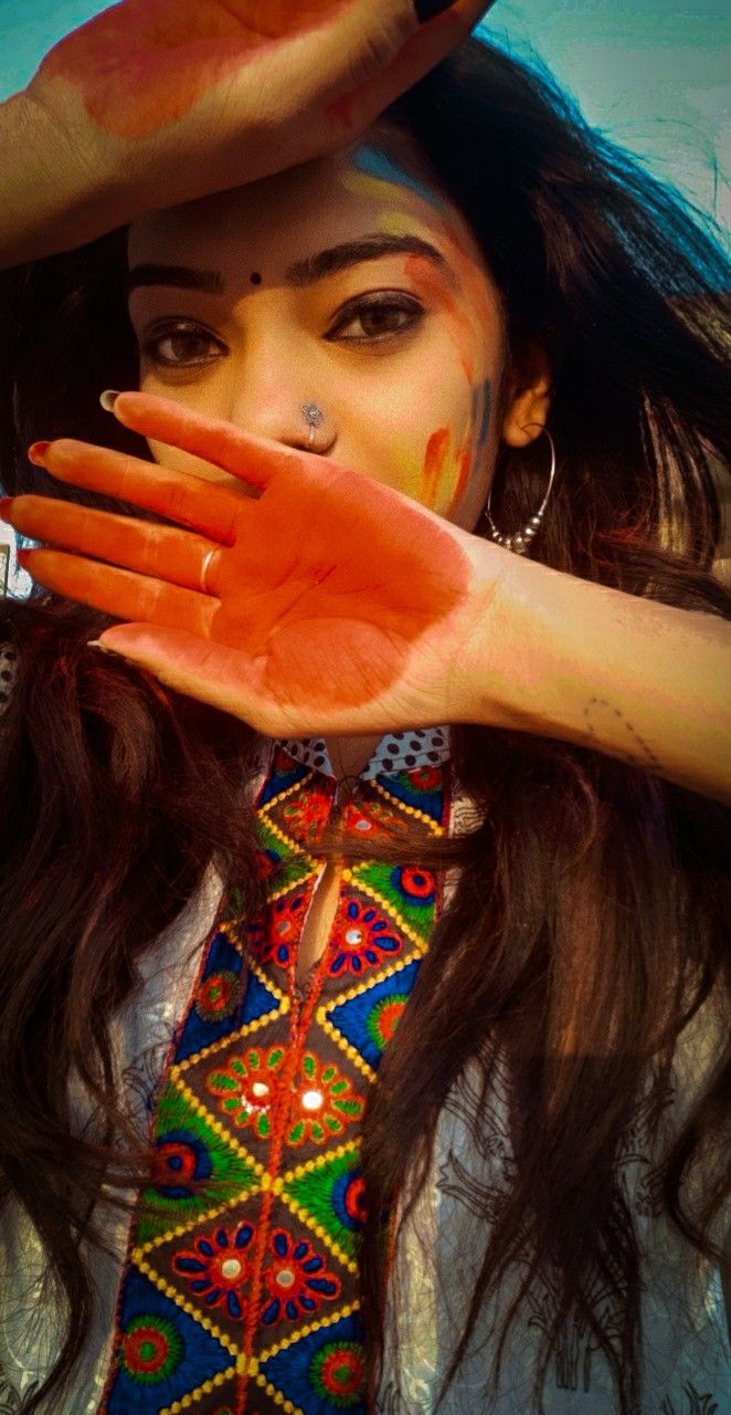 a woman with her hands on her face and painted body in bright colors is posing for the camera