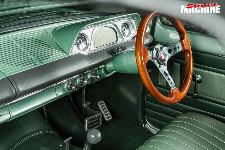 the interior of an old green car with wood steering wheel and dash board on display