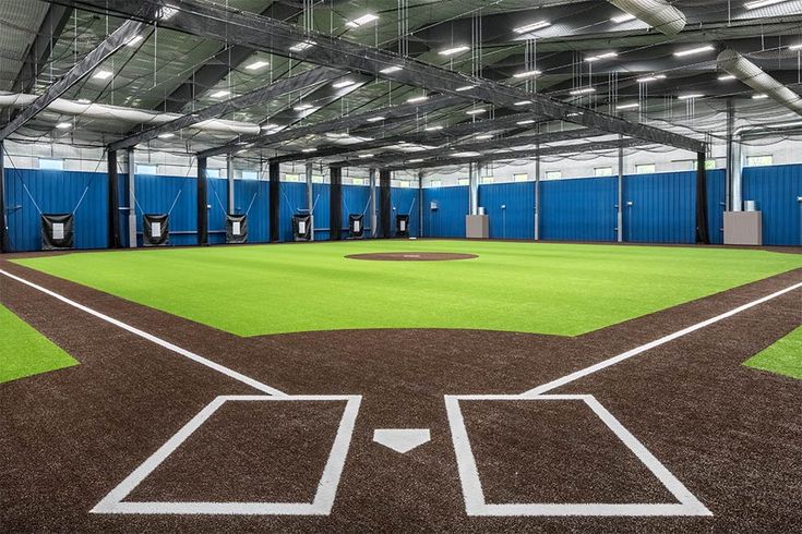 an indoor baseball field with blue walls and white lines on the grass is shown in this image