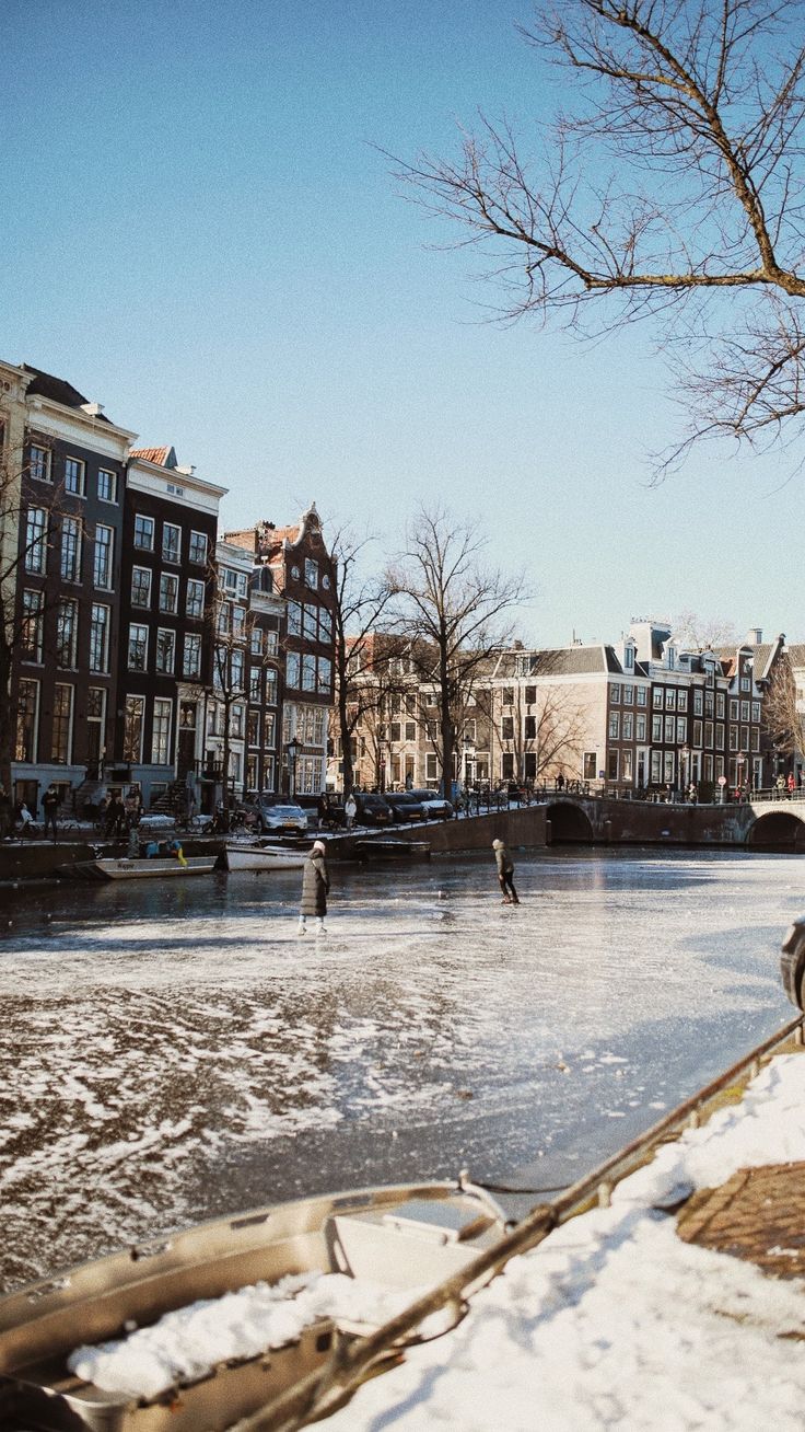 people are skating on an icy river in the middle of winter with buildings and boats