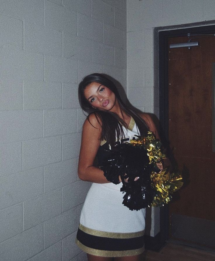 a woman in a white dress holding a black and gold cheerleader pom pom