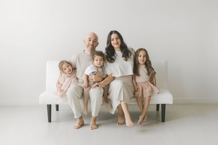 a family sitting on a white couch in front of a white wall, posing for the camera