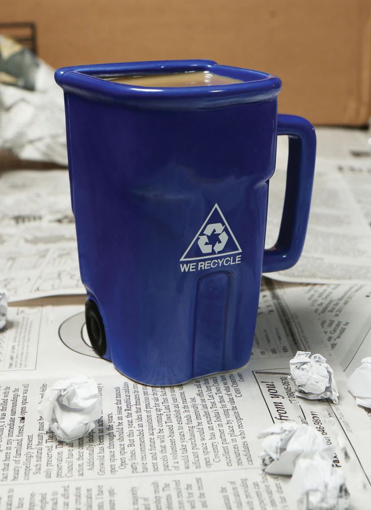 a blue trash can sitting on top of a table next to newspaper and crumpled paper