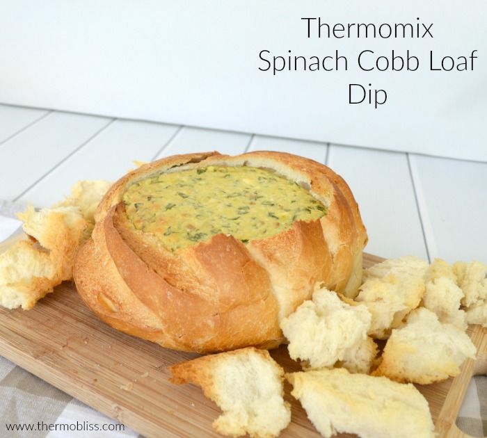 a bread bowl filled with spinach and cheese on a cutting board next to crackers