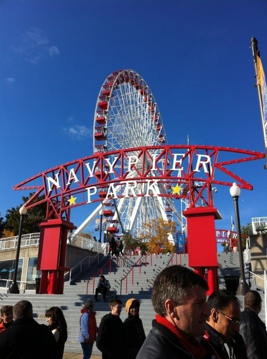 people are standing in front of an amusement park sign with a ferris wheel in the background