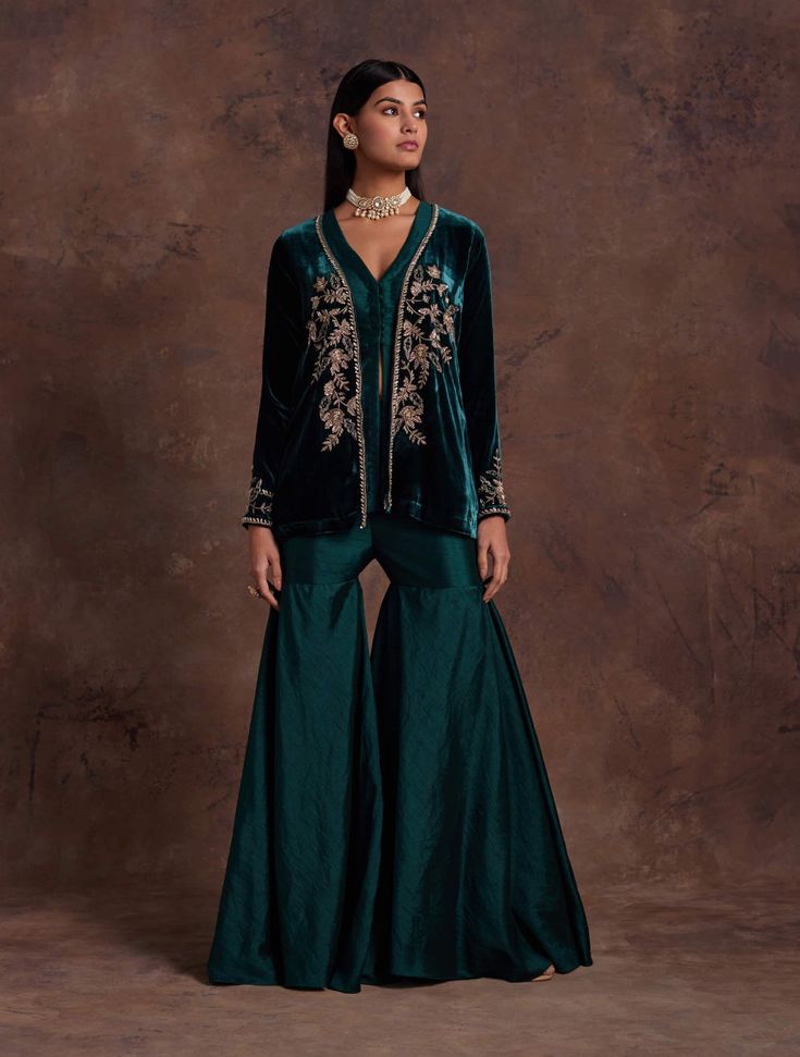 Editors Note Drape yourself in elegance with a green silk velvet jacket featuring hand embroidery at the front center and sleeves. Paired seamlessly with a silk peplum adorned with a V-neckline and potli buttons, along with complementing sharara pants, this ensemble exudes sophistication and style. Perfect for occasions where you seek a perfect balance of traditional craftsmanship and contemporary flair. Velvet Jacket Outfit, Sharara Outfits, Western Party Wear, Green Sharara, Jacket Lehenga, Editors Note, Indian Jackets, Green Velvet Jacket, Sharara Designs