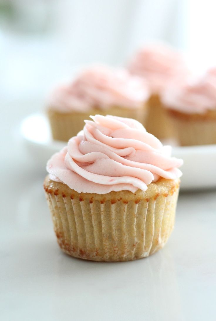 two cupcakes with pink frosting sitting on a white plate next to each other