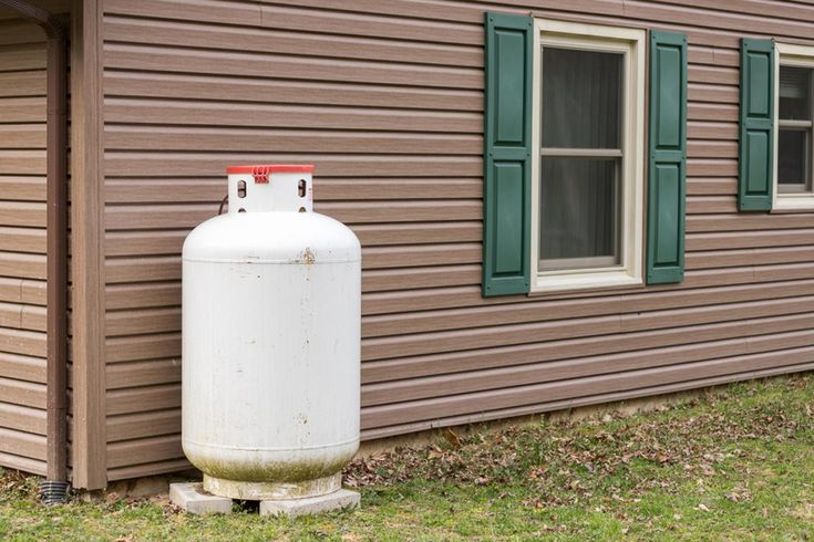 an old propane tank sitting in front of a brown house with green shutters