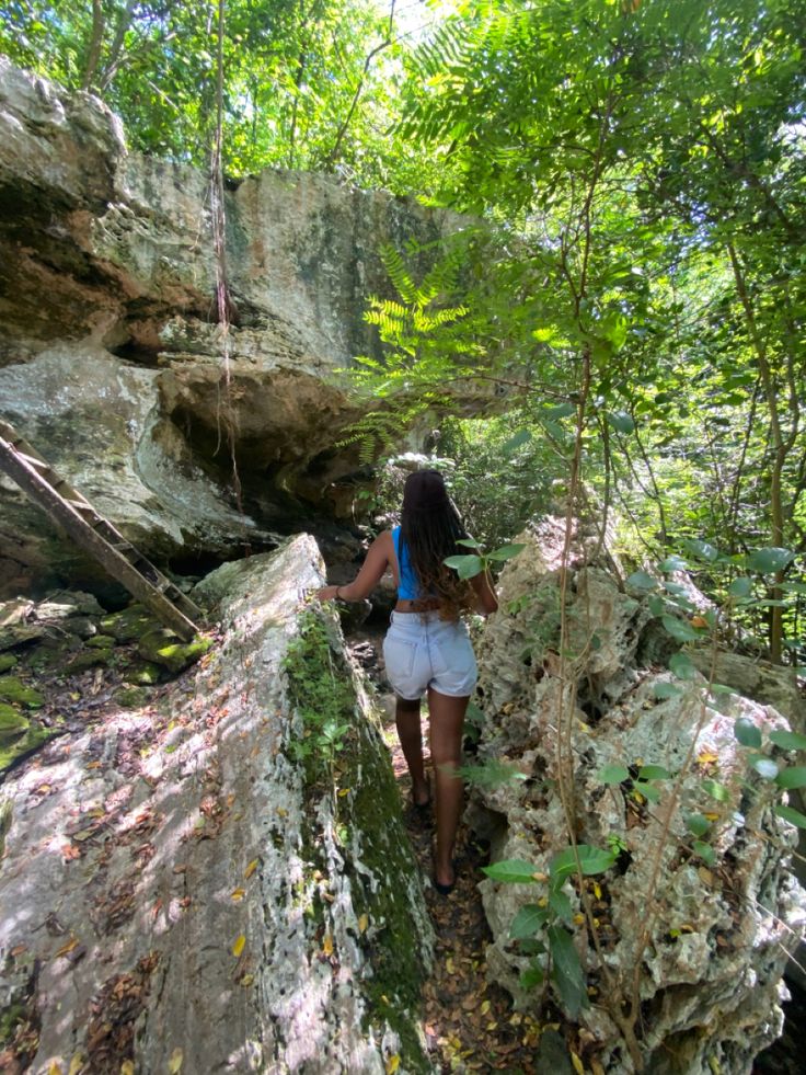 a woman is walking on the rocks in the woods with her back to the camera