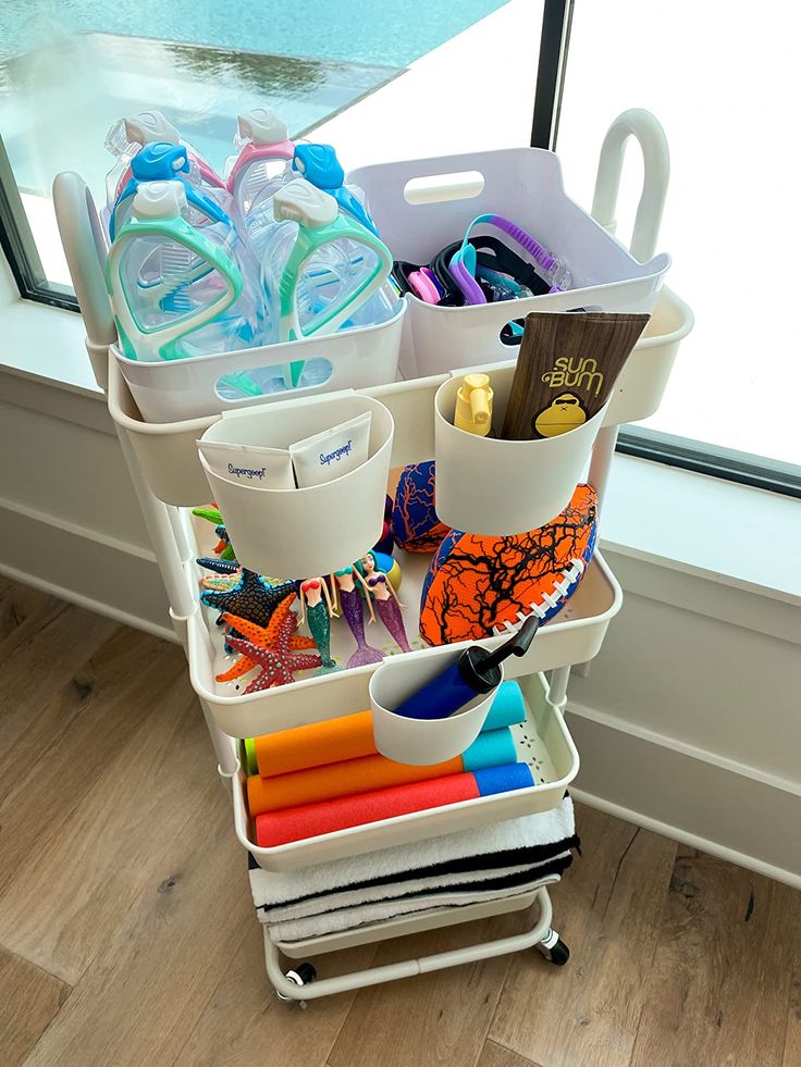 a cart filled with lots of different items next to a window on a hard wood floor