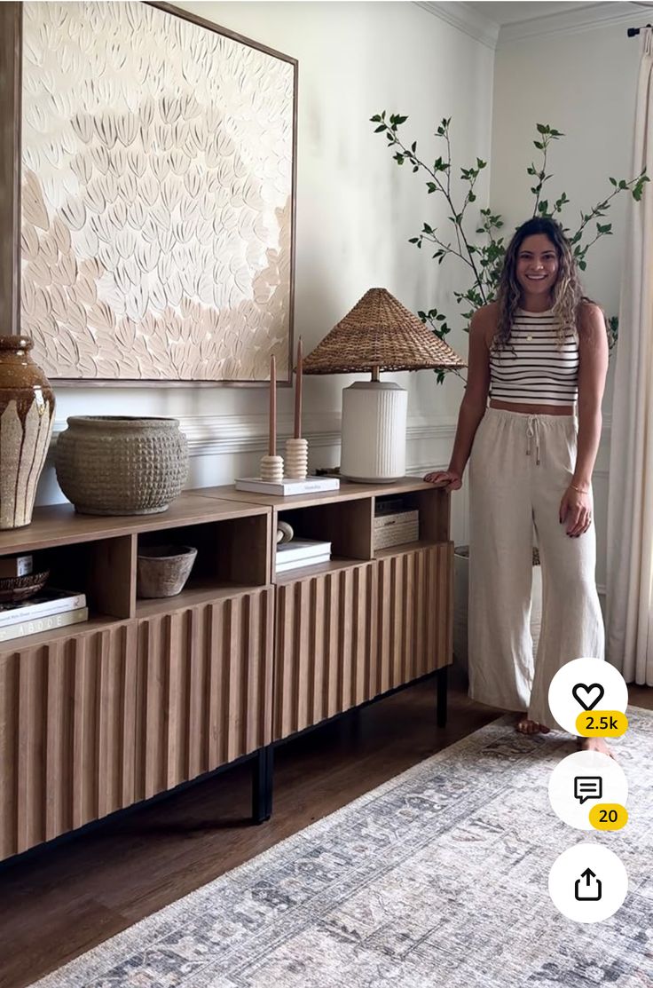 a woman standing in front of a large painting on a wall next to a wooden cabinet