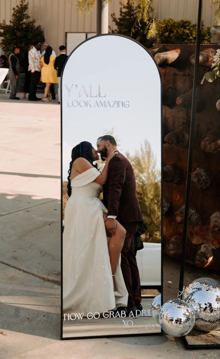 a man and woman kissing in front of a large mirror with silver balls around it