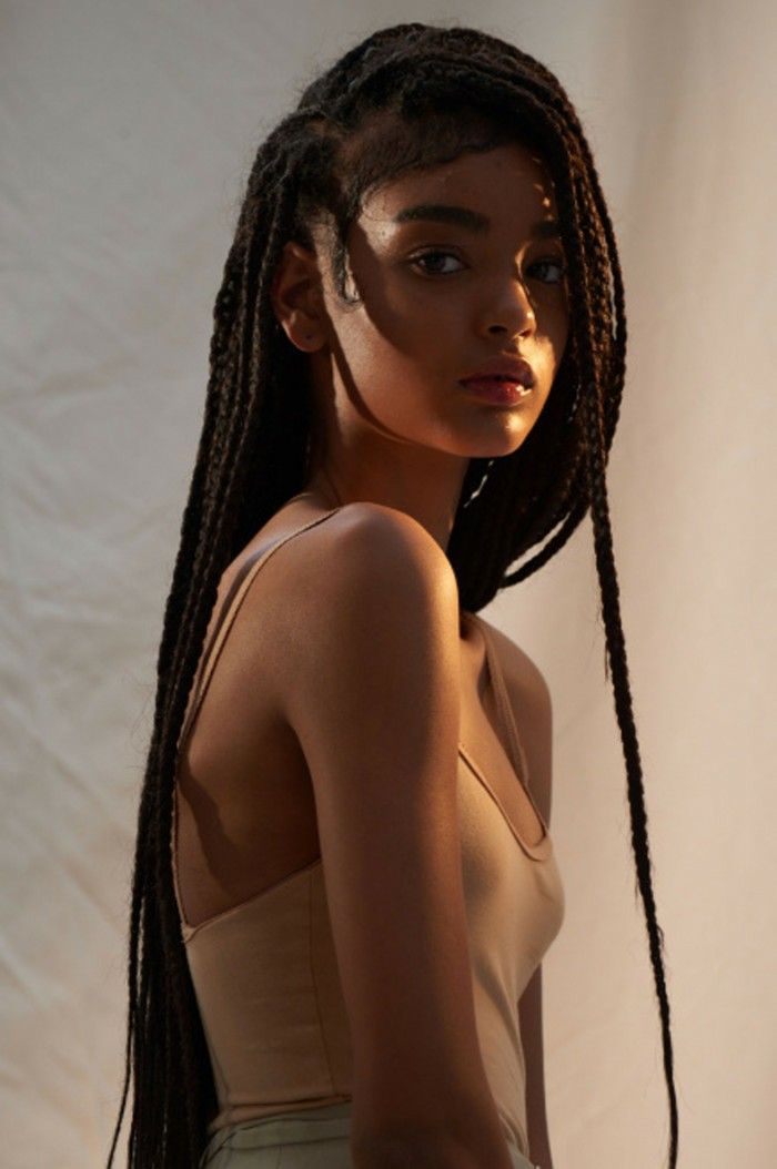 a woman with long braids standing in front of a white backdrop