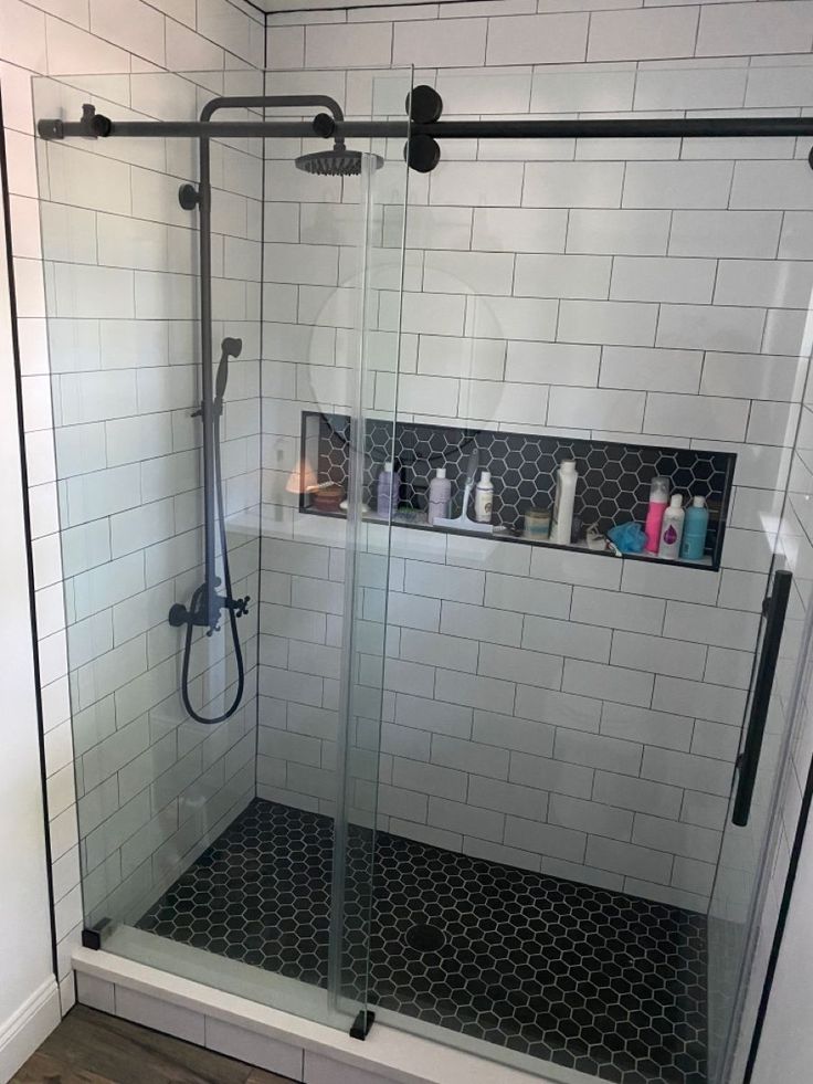 a walk in shower sitting next to a white tiled wall with black grouting