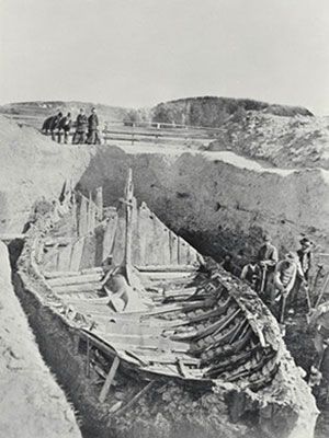 an old black and white photo of people standing on the shore next to a boat