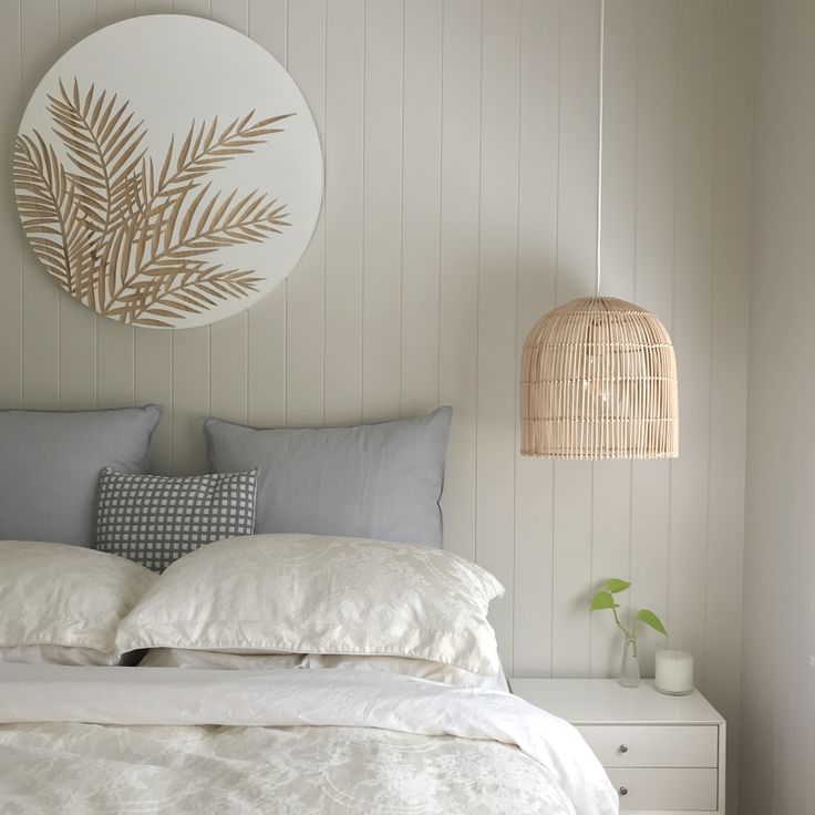 a bed with white linens and pillows in a bedroom next to a wicker lamp