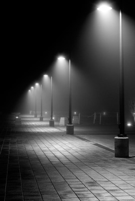 black and white photograph of street lights in the foggy night with no one on it