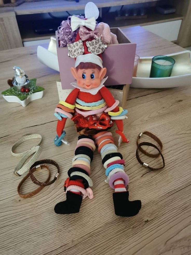 an elf doll sitting on top of a wooden table next to some scissors and other items