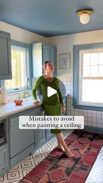 a woman standing in a kitchen with her hand on the counter and looking up at the ceiling