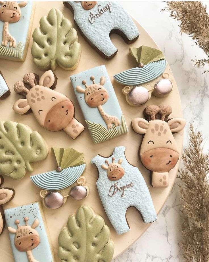 decorated cookies with giraffes and leaves are on a plate next to dried grass