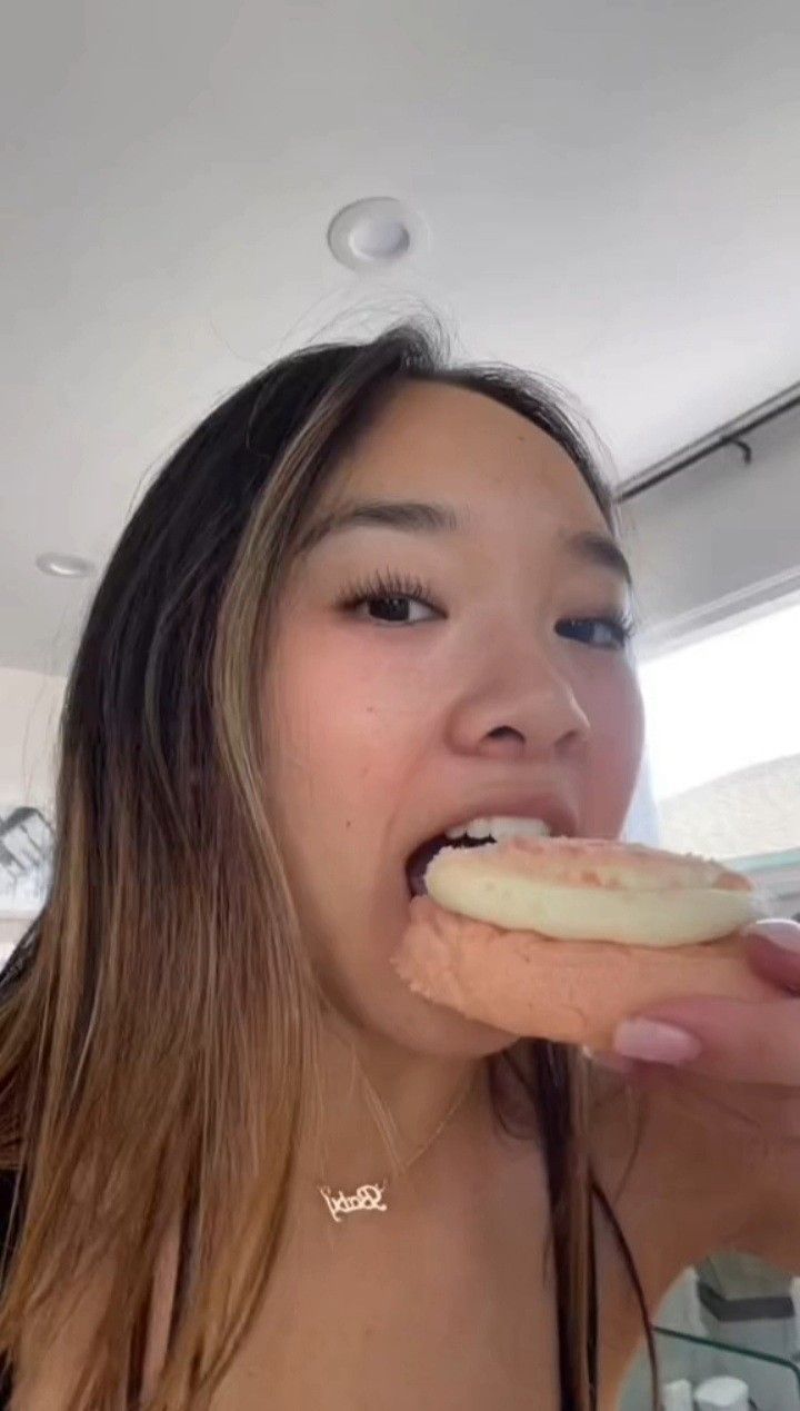 a woman is taking a bite out of a hot dog with icing on it