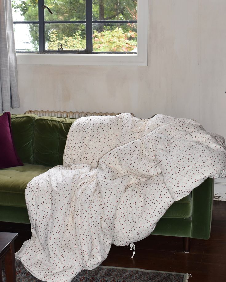 a living room with a green couch and white blanket on it's back, in front of a window