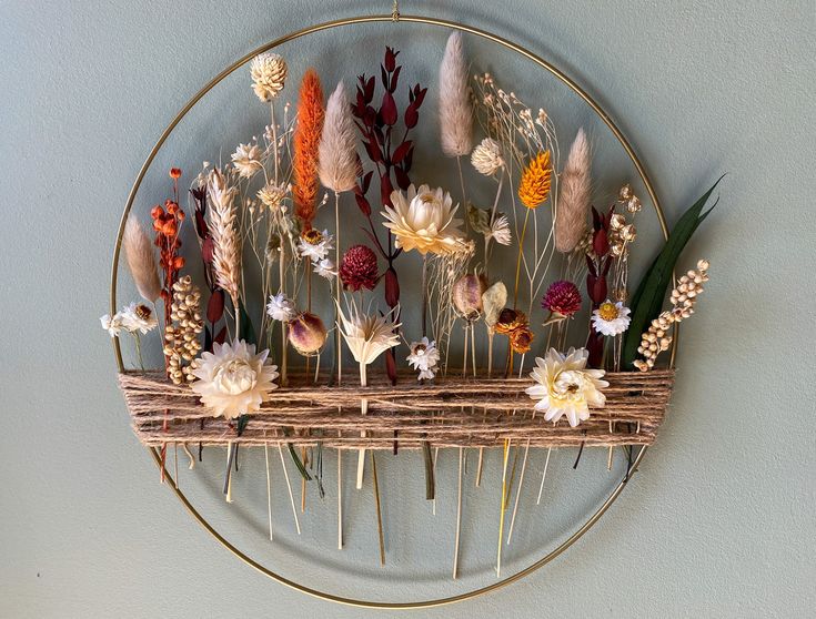 an arrangement of dried flowers on a circular metal wall decoration with branches and grass in the center