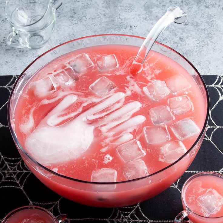 a glass filled with ice sitting on top of a table next to two cups and spoons