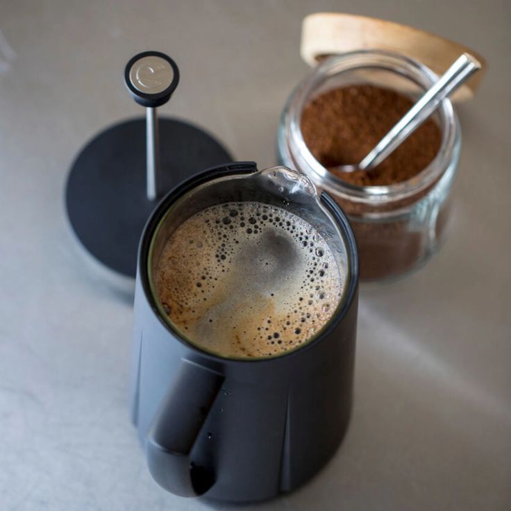 there is a coffee maker next to a cup with some liquid in it and two spoons on the table