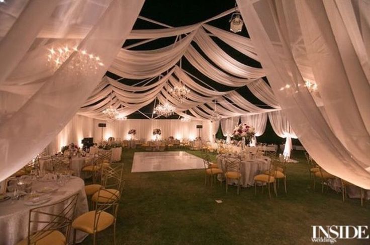 the inside of a tent with tables and chairs set up for a formal function at night