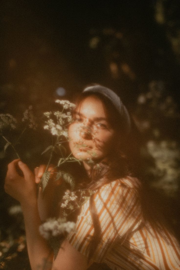 a woman holding a flower in her hand and looking up at the sun shining on her face