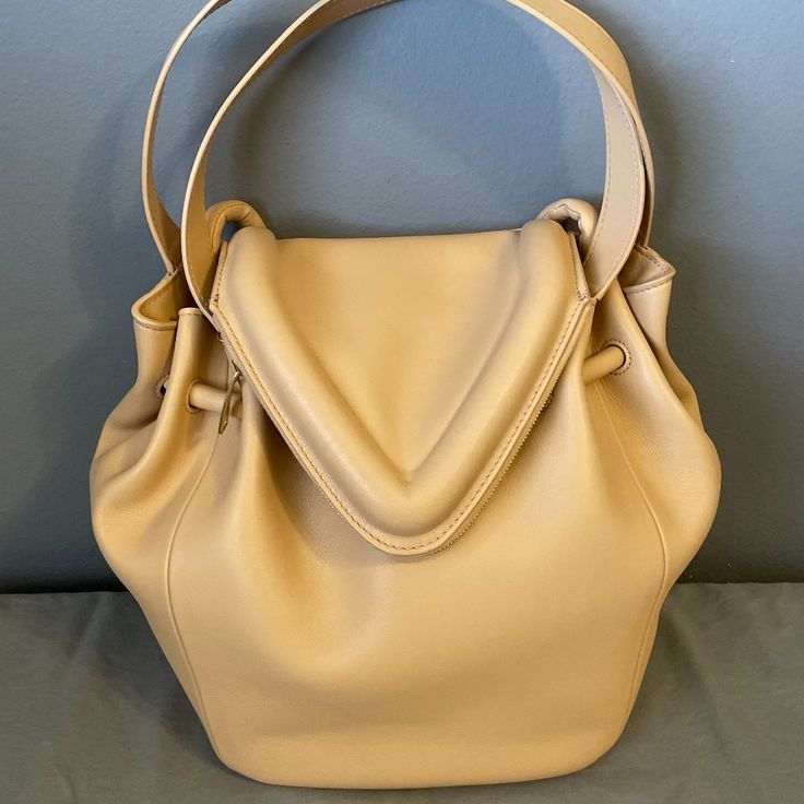 Beige ‘Beak’ Shoulder Bag From Bottega Veneta. Crafted From Calf Leather, This Design Cinches Closed With A Drawstring And Features A Magnetic Closure, A Fold-Over Front With A Pocket With A Two-Way Zip Fastening, A Shoulder Strap, Two Half-Round Handles, Gold-Tone Metal Hardware And One Internal Compartment With A Slip Pocket. Beak Bag With V-Shape Flap Bottega Veneta Art. 666531 Vcp40 2700 Color:Almond Gold 100% Calf Leather Height: 24cm Width: 28cm Model's Measurements Height: 176cm Bust: 85c High-end Beige Bucket Bag, Luxury Beige Pouch Bucket Bag, High-end Everyday Pouch Bucket Bag, Luxury Beige Hobo Bag With Dust Bag, Luxury Beige Top Handle Hobo Bag, Luxury Beige Hobo Bag With Top Handle, Luxury Beige Pouch Hobo Bag, Luxury Beige Shoulder Bucket Bag, Designer Beige Satchel Bucket Bag