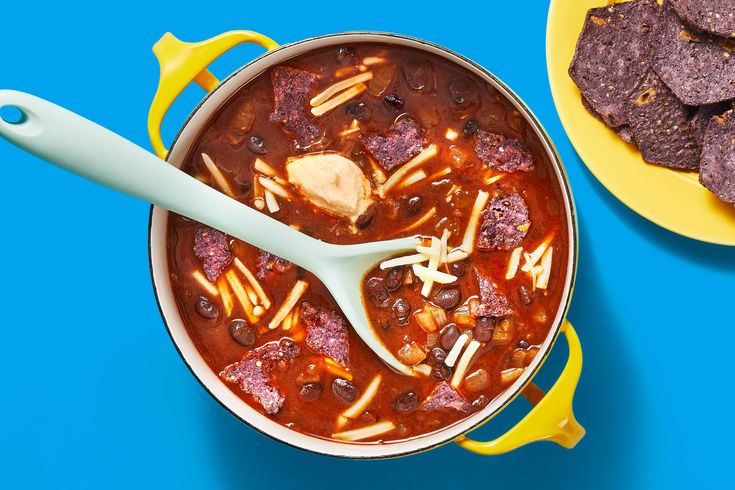 a bowl of chili and tortilla chips on a blue table with a yellow plate