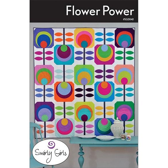 a colorful flower quilt hanging on a wall next to a blue table with a vase