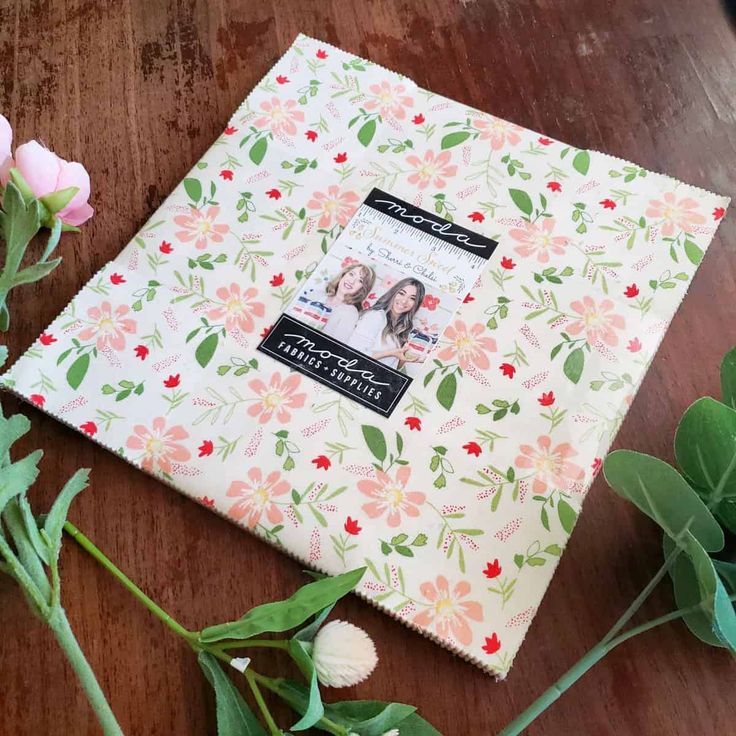 a photo album with flowers and greenery next to it on a wooden table top