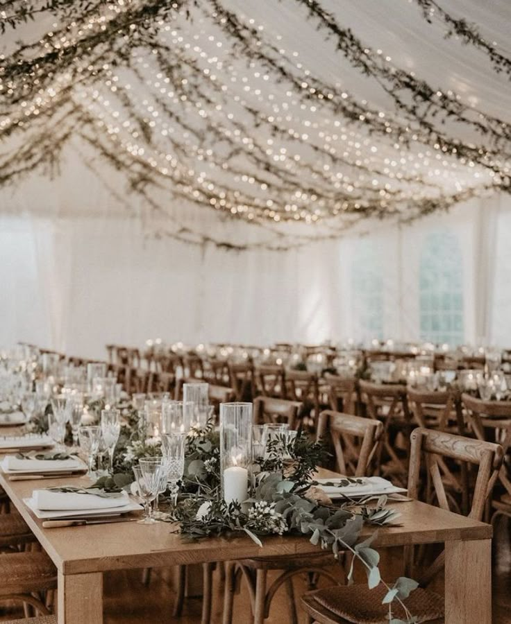 the tables are set up with candles and greenery for an elegant wedding reception in a marquee