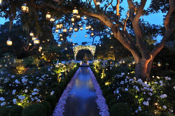 an outdoor wedding with lanterns and flowers on the path to the ceremony venue at night