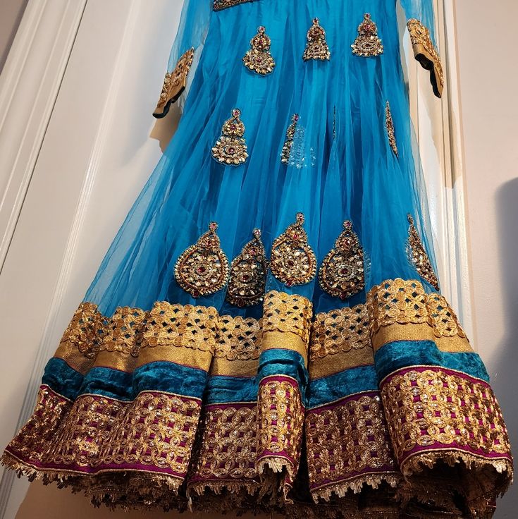 This Is An Amazing Blue Anarkali Dress With Matching Pants And Scarf. The Fabric Has Shining Gold Accents. This Will Make A Great Choice For Any Occasion. Blue Festive Anarkali Set With Traditional Drape, Festive Blue Anarkali Set With Traditional Drape, Blue Anarkali Set For Festive Occasions, Blue Anarkali Set With Sheer Dupatta For Navratri, Blue Churidar With Sheer Dupatta For Navratri, Blue Anarkali Set With Sheer Dupatta For Festivals, Blue Bollywood Anarkali Set For Designer Wear, Festive Blue Anarkali Set, Blue Maxi Length Sharara With Cutdana