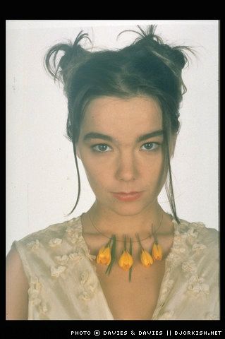 a woman with flowers in her hair wearing a white top and yellow necklace on her neck