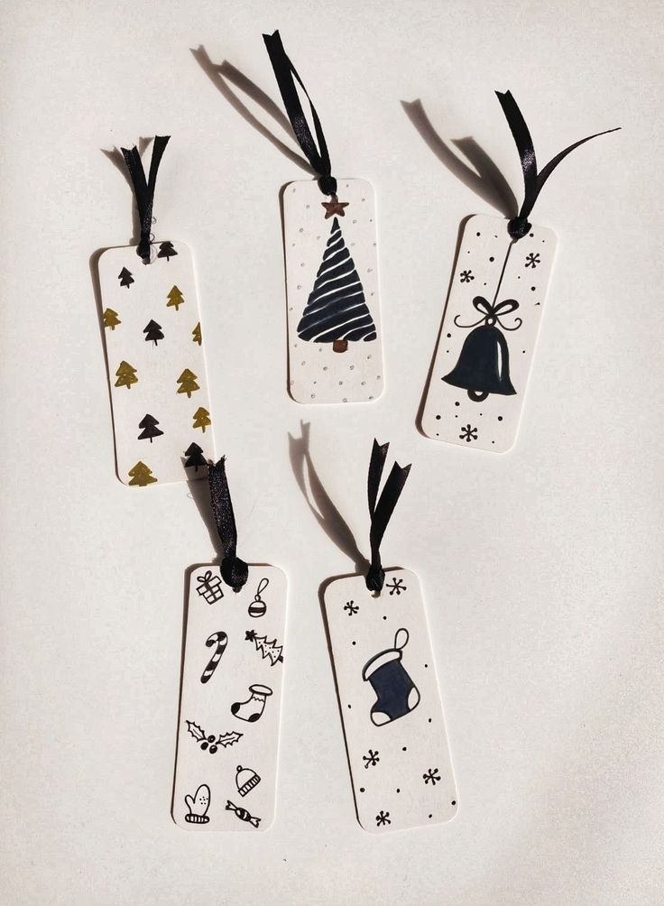 four tags with different designs on them are hanging from black ribbon and decorated with christmas decorations