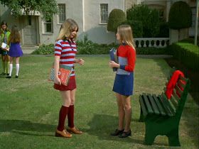 two young women standing next to each other in front of a building and one holding a red purse