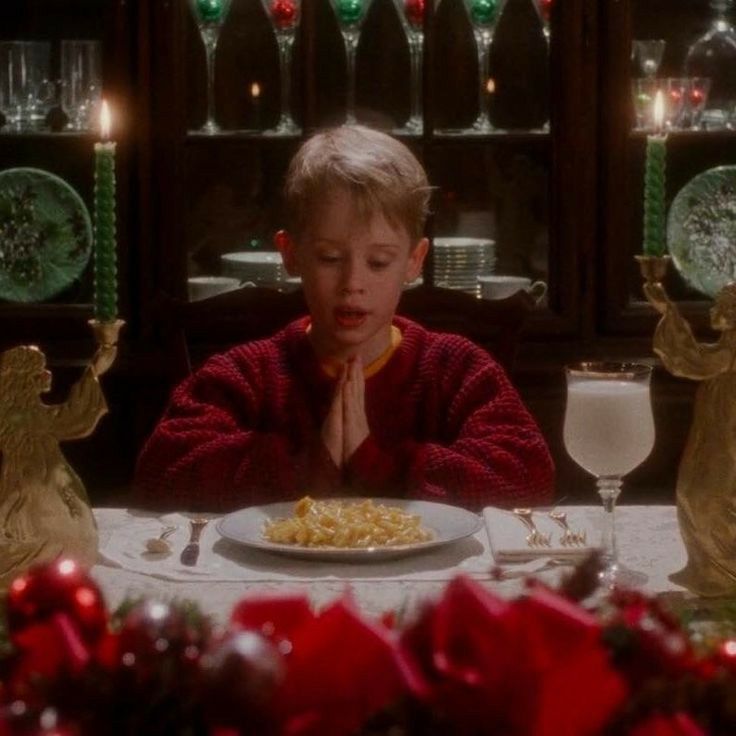 a young boy sitting at a table with food in front of him and christmas decorations around him