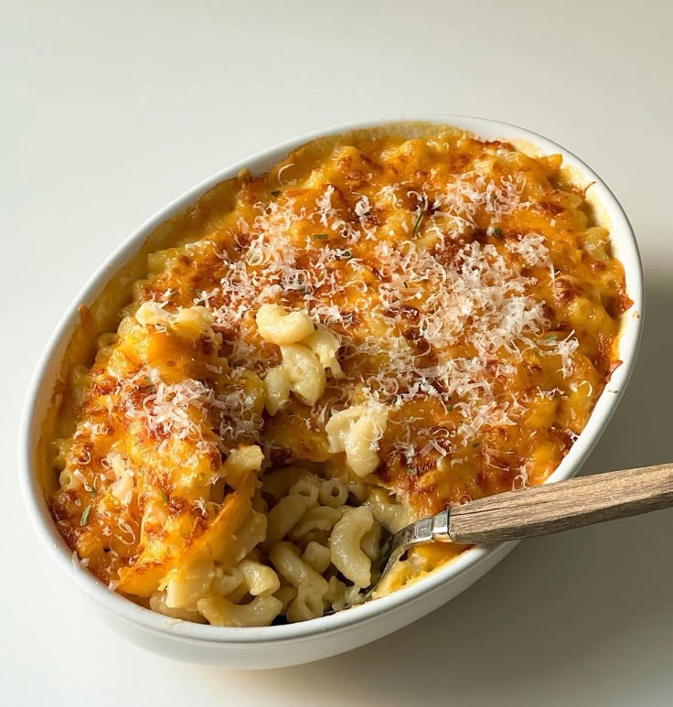 a bowl filled with macaroni and cheese on top of a white table next to a wooden spoon