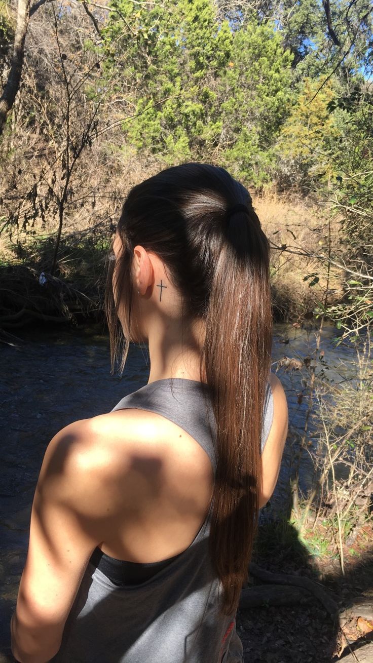 a woman standing in front of a river with her back turned to the camera, wearing a gray tank top